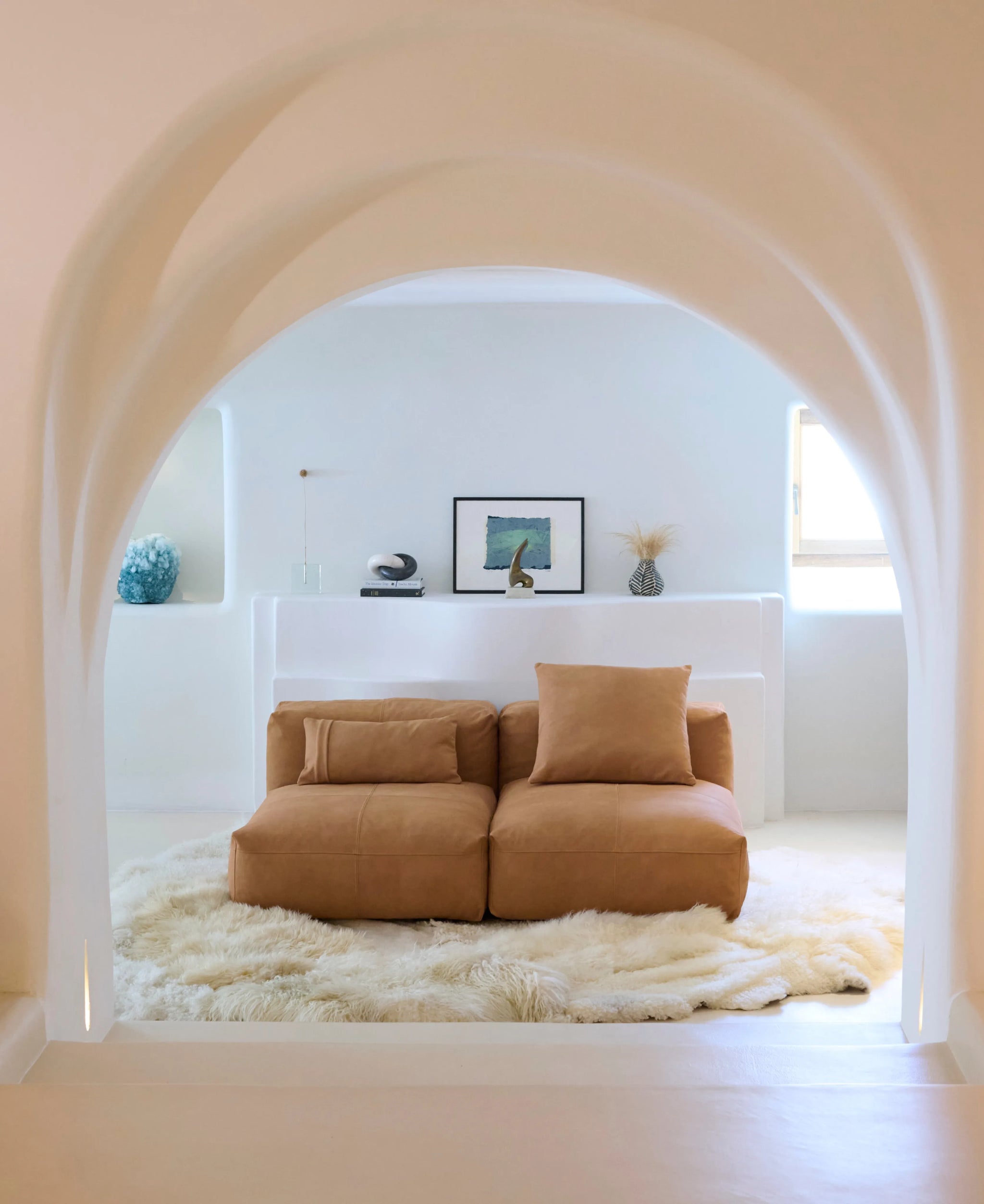 Minimalistisches Wohnzimmer mit cognacfarbenem Vetsak Sofa, weißem Interieur und dekorativen Wohnaccessoires.