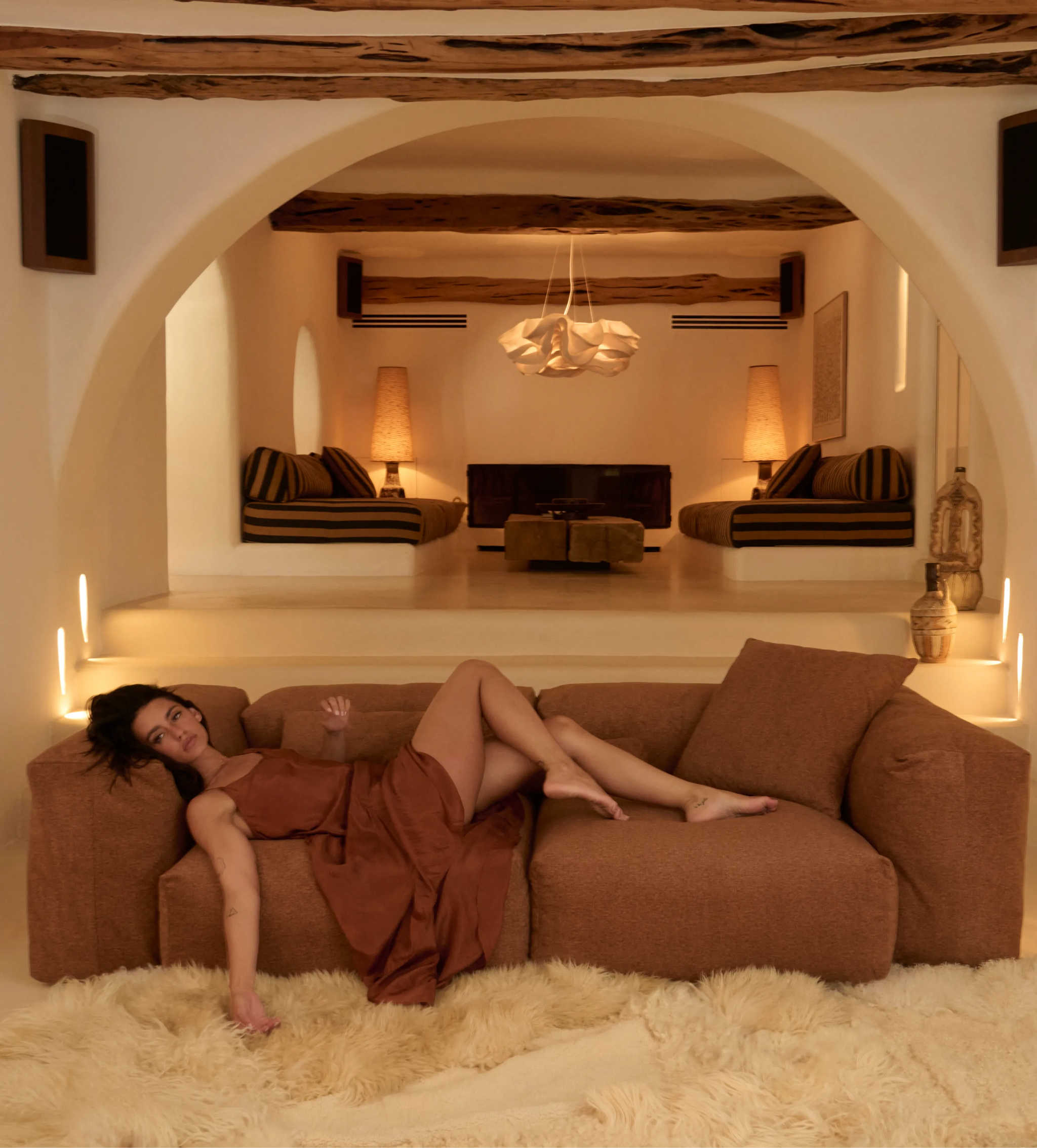 Person entspannt auf einem braunen vetsak Sofa in einem warm beleuchteten Wohnzimmer mit Rundbögen und Designinterieur.